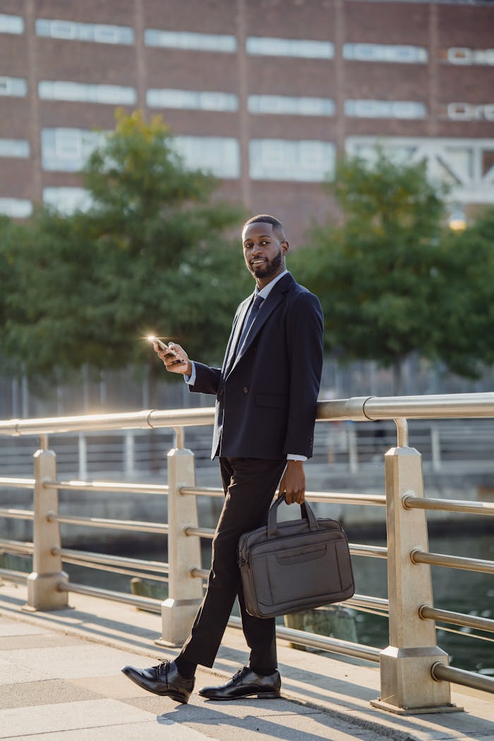 Professional in business attire using smartphone while walking on bridge in city setting.